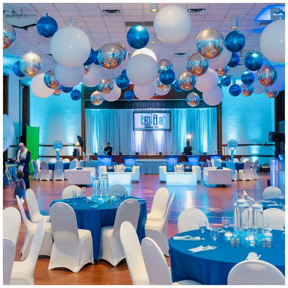 silver, white, and blue balloons individually hung from ceiling above circular tables and dance floor.