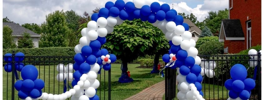 A blue and white balloon arch over a fence gate walkway that is strung to a blue and white column on either side.