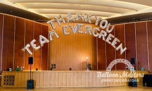 Silver balloons arched over a stage that say "Than you Team Evergreen".