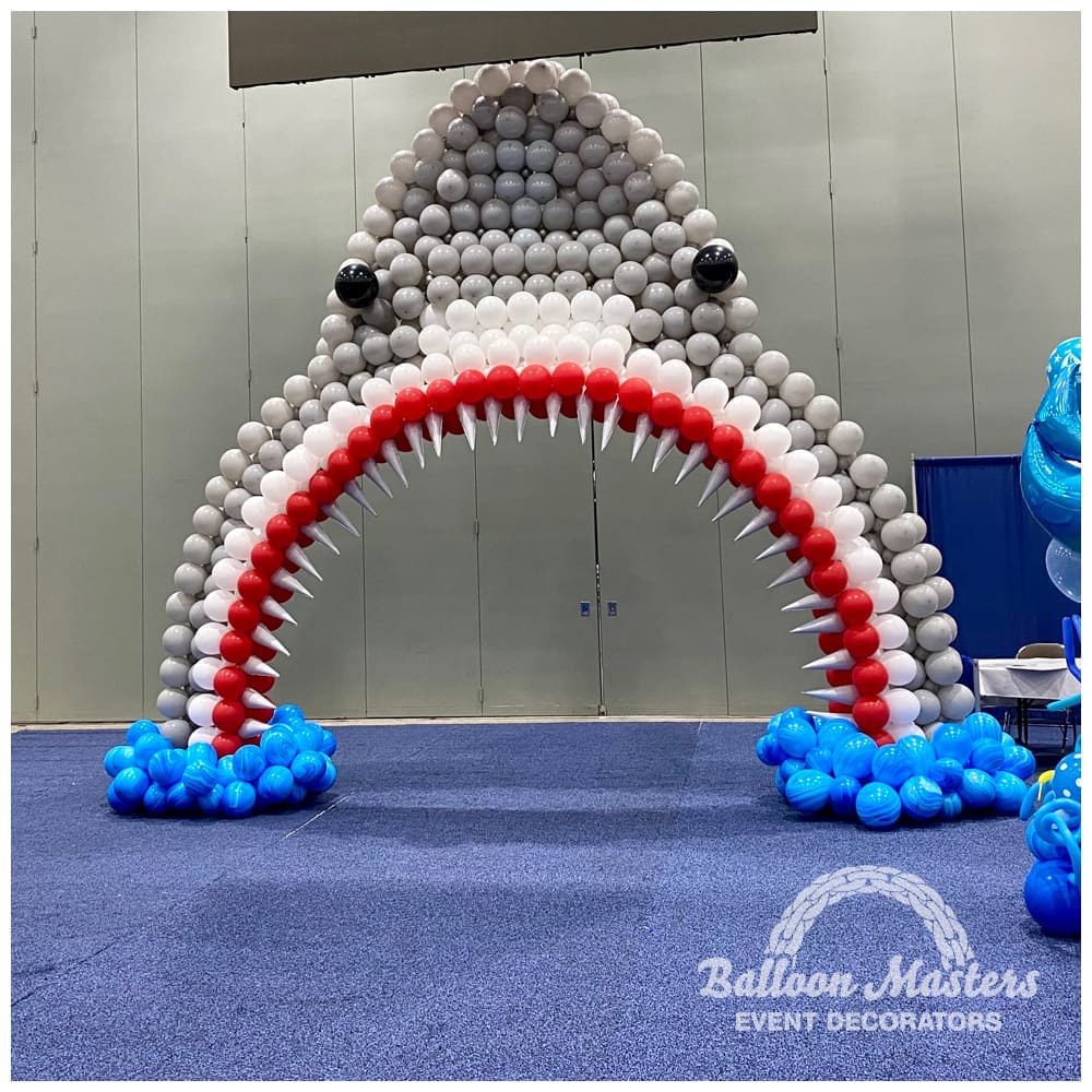 gray white and red balloon arch, shaped to resemble shark head.